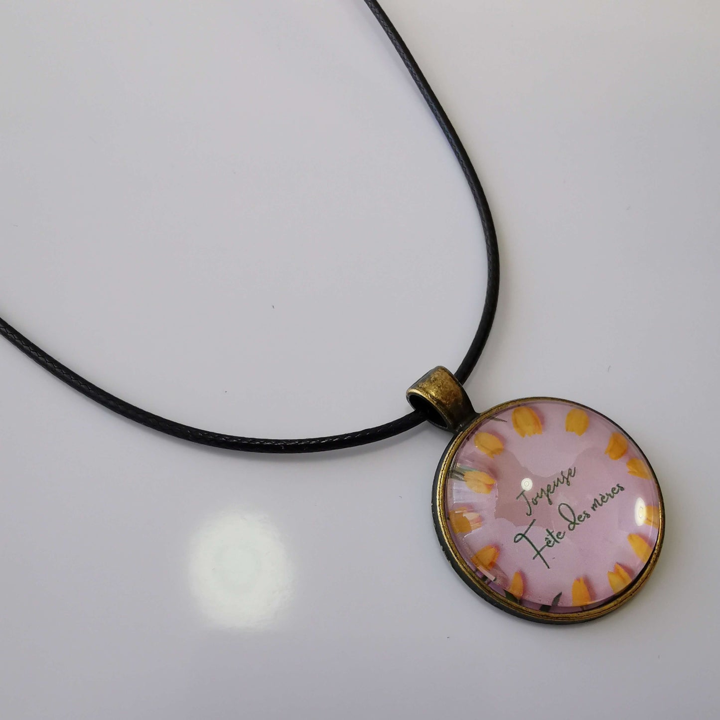 Memdalz bijou personnalisé avec vidéo et photo spéciale pour la fête des mères. Sur ce modèle est inscrit "Joyeuse fête des mères" en calligraphie de couleur vert sur un fond rose entouré de tulipes jaunes.